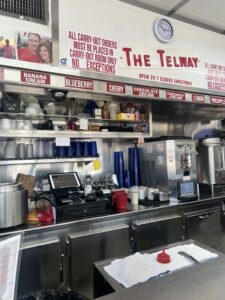 Inside The Telway restaurant in Detroit, showing the counter, menu signs for pies, and kitchen equipment. Known for classic coney dogs, Telway is a must-visit local spot.