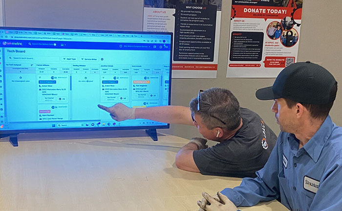 Two men looking at a large screen of service and repair jobs