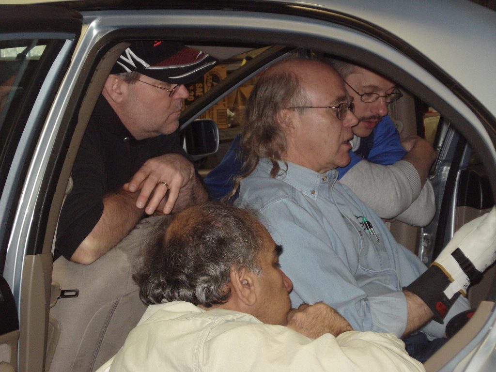 A trainer with three students giving hands on training inside a car.