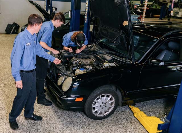 Three students looking under the hood of a black vehicle.